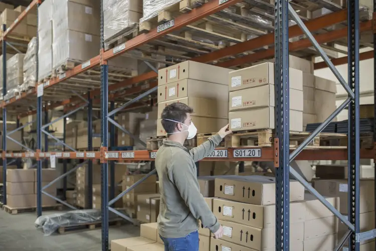 man-wearing-mask-holding-boxes-shelf-warehouse.jpg